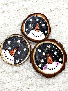 three wooden slices with painted snowmen on them sitting on a white carpeted surface