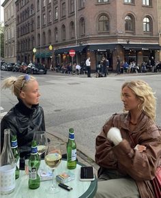 two women sitting at an outdoor table talking to each other in front of a building