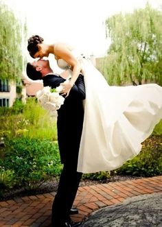 the bride and groom are kissing in front of some green trees with their arms around each other