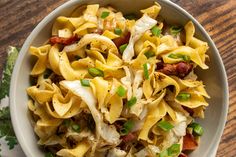 a white bowl filled with pasta and meat on top of a wooden table next to a green napkin