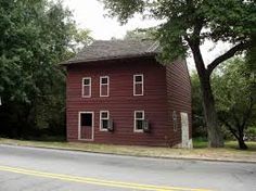 a red house sitting on the side of a road next to some trees and grass