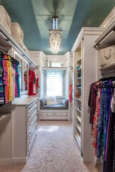 a walk in closet with lots of clothes hanging on the walls and drawers, along with a chandelier