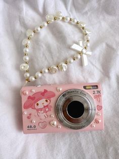 a pink camera sitting on top of a bed next to a white cross and pearl necklace