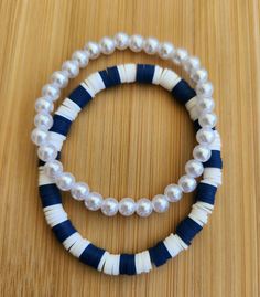 two bracelets with white and blue beads on top of a wooden table next to each other