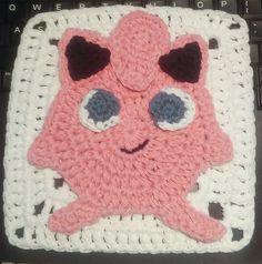 a crocheted square with an image of a pink creature on it's face