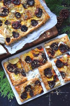 two pans filled with pizza sitting on top of a wooden table next to pine cones