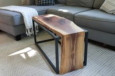 a wooden table sitting on top of a metal frame in front of a gray couch