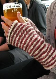 a person holding a beer in their hand while sitting on a bench with other people