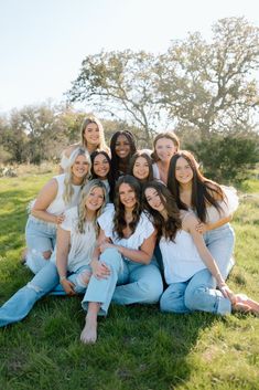 a group of young women sitting on top of a lush green grass covered field with trees in the background