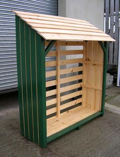 a green and wooden storage shed sitting on the side of a road next to a building