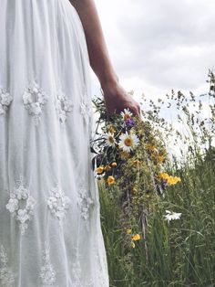 a woman in a white dress holding a bouquet of wildflowers and daisies