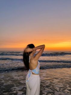 a woman standing on top of a sandy beach next to the ocean at sun set