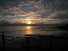 the sun is setting over the ocean with clouds in the sky