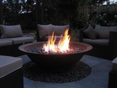 a fire pit sitting on top of a patio next to couches and tables with pillows