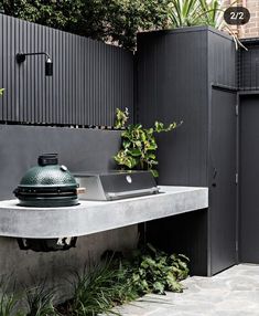 an outdoor bbq grill in front of a black fence and green plants on the side