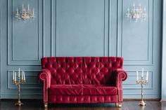 a red couch sitting in front of a wall with chandeliers on either side