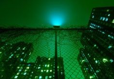 an image of a green light in the night sky from behind a chain link fence