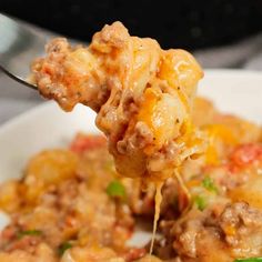 a close up of a spoon full of food with meat and cheese on it's side