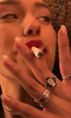 a close up of a person with rings on her fingers and holding something in their mouth