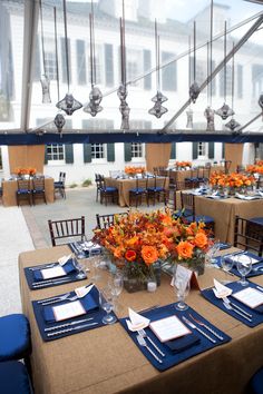 an indoor dining area with blue and orange table cloths, place settings and centerpieces