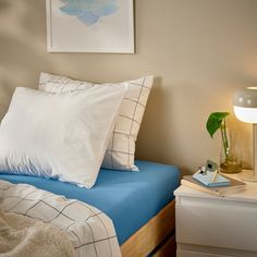 a bed with white pillows and blue sheets in a small room next to a lamp