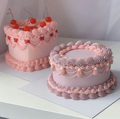 two pink cakes sitting on top of a white table next to each other with cherry toppings