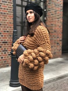 a woman is standing on the sidewalk wearing a brown sweater and black tights