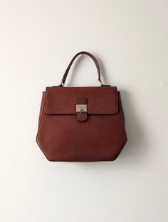 "Lancel top handle handbag from the 1970s in a beautiful buttery maroon leather. Adorable albeit unusual hexagonal shape for such a classic-looking bag. Gold hardware. Spacious leather interior compartment with one zip pocket and one slip pocket.  The bag suffers from several flaws: the leather shows many scratches, especially on the front. There is wear at the corners. The gold hardware is tarnished and the top handle is crooked. The bag has loops for a strap, but the shoulder strap is missing. Braided Bag, Maroon Leather, Top Handle Bags, Top Handle Handbags, The 1970s, Shoulder Purse, Leather Interior, Leather Purses, Leather Tote