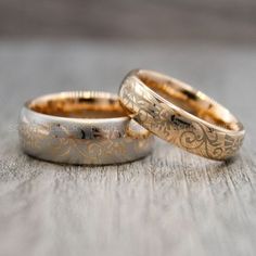 two gold wedding rings sitting next to each other on top of a wooden table,