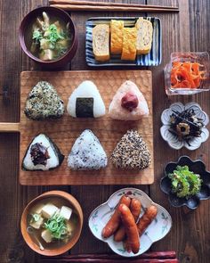 an assortment of sushi on a wooden tray with chopsticks and small bowls