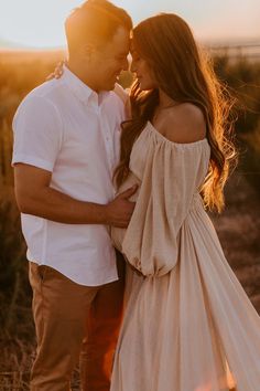 a man and woman standing in the desert at sunset with their arms around each other