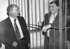 two men in suits are standing behind bars and smiling at each other as they talk