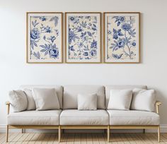 two blue and white floral paintings hang above a couch in a room with hardwood floors