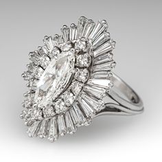 This elegant diamond ballerina ring is centered with one (1) marquise brilliant cut diamond weighing 0.79 carats that is set into a six-prong setting. The center diamond is bordered with fourteen (14) prong set round brilliant cut diamonds, and thirty-two (32) prong set tapered baguette cut diamonds. The ring measures 26.1mm at the top, rises 11.3mm above the finger, tapering to 1.9mm wide and 1.8mm thick at the base of the shank. It is crafted in platinum and is currently a size 7.25. Gia Certified Marquise Diamond Ring, Elegant Gia Certified Marquise Wedding Ring, White Marquise Cut Gia Certified Diamond Ring, Gia Certified Marquise Diamond Ring Fine Jewelry, Gia Certified Marquise White Gold Diamond Ring, Gia Certified Marquise Platinum Rings, Gia Certified Platinum Marquise Rings, Gia Certified Marquise Diamond Ring For Anniversary, Gia Certified Marquise Diamond Ring For Wedding