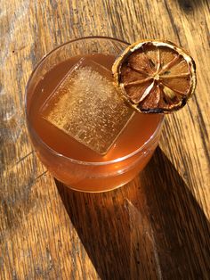 a drink in a glass with an orange slice on the rim sitting on a wooden table