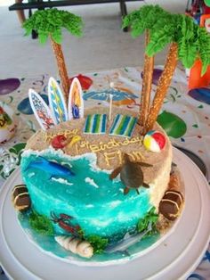 a decorated birthday cake with surfboards and palm trees on the top is sitting on a table