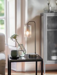 a table with a lamp and vase on it in front of a couches window