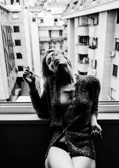 a woman sitting on top of a window sill next to a cityscape