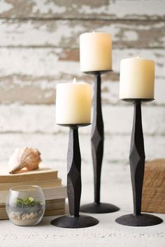 three candles sitting next to each other on top of a wooden table with shells and books