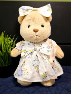 a brown teddy bear wearing a white dress and holding a small bunny in it's hand