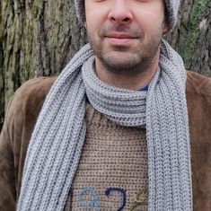 a man wearing a knitted hat and scarf next to a tree with his eyes closed