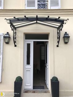 the front entrance to a house with white shutters and black planters on either side