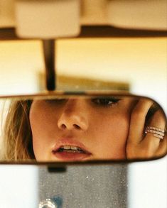 a woman looking at her reflection in the rear view mirror while she is holding her hand to her ear