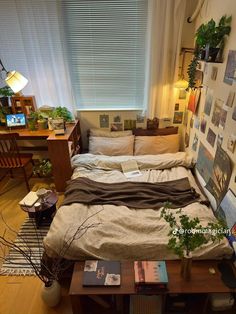 an unmade bed in a small room with plants and pictures on the wall