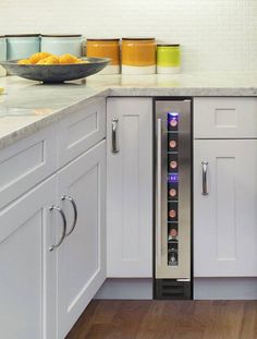 a wine cooler in the middle of a kitchen with white cabinets and wood flooring