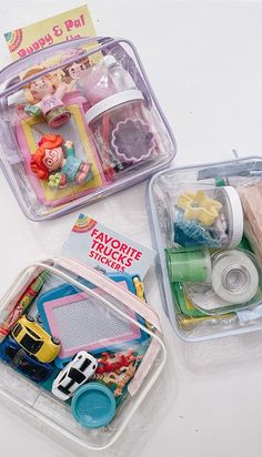 two plastic containers filled with toys on top of a white table next to each other