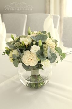 a vase filled with white flowers and greenery on top of a dining room table