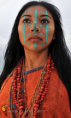 a woman with blue paint on her face and chest, standing in front of the ocean