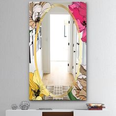 a mirror hanging on the wall above a white cabinet with flowers painted on it and an open door