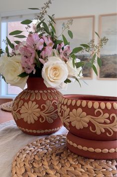 two vases with flowers in them sitting on a woven placemat next to each other